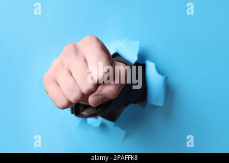 Ein Geschäftsmann, der mit der Faust durch hellblaues Papier bricht, eine Nahaufnahme Stockfoto