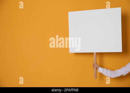 Frau mit leerem Schild auf gelbem Hintergrund, Nahaufnahme. Platz für Text Stockfoto