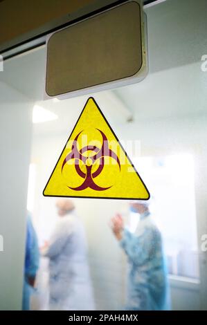 Warnschild „Biogefährdung“ auf durchsichtiger Labortür Stockfoto