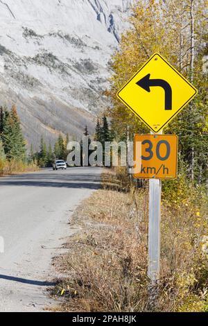 Hellgelbe und orangefarbene Straßenschilder mit Warnung vor bevorstehender Kurve und Geschwindigkeitsbegrenzung von 30 km/h auf einer Autobahn im Jasper National Park, Kanada. Stockfoto