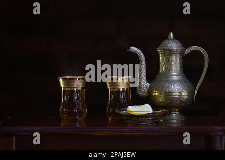 Eine klassische, feierliche, kunstvoll verzierte türkische Teekanne und Gläser mit sanfter, dunkler Stimmungsbeleuchtung und Kopierbereich auf der linken Seite Stockfoto