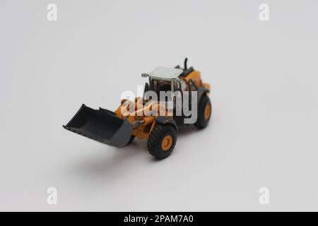 Nahaufnahme eines orangefarbenen Miniatur-Spielzeugs mit Radlader, isoliert auf weißem Hintergrund. Konzeptfoto eines schweren Miniaturspielzeugs. Stockfoto