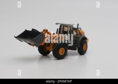 Nahaufnahme eines orangefarbenen Miniatur-Spielzeugs mit Radlader, isoliert auf weißem Hintergrund. Konzeptfoto eines schweren Miniaturspielzeugs. Stockfoto
