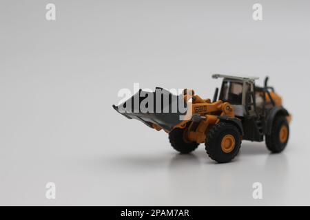 Nahaufnahme eines orangefarbenen Miniatur-Spielzeugs mit Radlader, isoliert auf weißem Hintergrund. Konzeptfoto eines schweren Miniaturspielzeugs. Stockfoto
