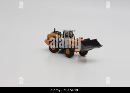 Nahaufnahme eines orangefarbenen Miniatur-Spielzeugs mit Radlader, isoliert auf weißem Hintergrund. Konzeptfoto eines schweren Miniaturspielzeugs. Stockfoto