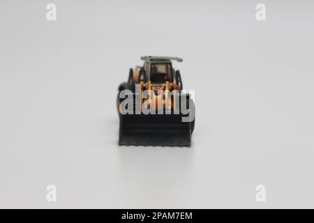 Nahaufnahme eines orangefarbenen Miniatur-Spielzeugs mit Radlader, isoliert auf weißem Hintergrund. Konzeptfoto eines schweren Miniaturspielzeugs. Stockfoto