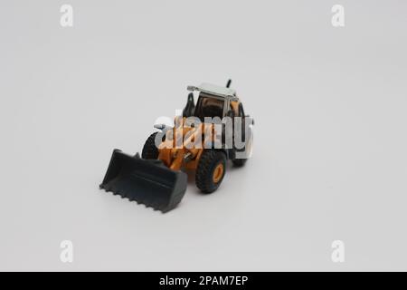 Nahaufnahme eines orangefarbenen Miniatur-Spielzeugs mit Radlader, isoliert auf weißem Hintergrund. Konzeptfoto eines schweren Miniaturspielzeugs. Stockfoto
