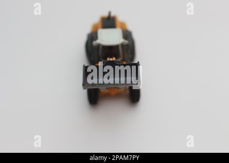 Nahaufnahme eines orangefarbenen Miniatur-Spielzeugs mit Radlader, isoliert auf weißem Hintergrund. Konzeptfoto eines schweren Miniaturspielzeugs. Stockfoto