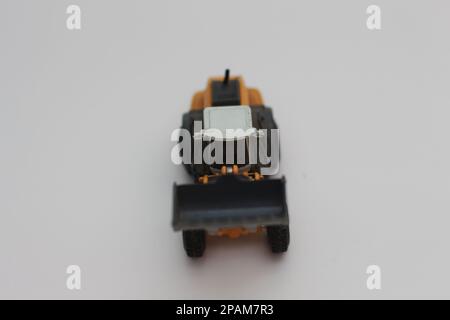Nahaufnahme eines orangefarbenen Miniatur-Spielzeugs mit Radlader, isoliert auf weißem Hintergrund. Konzeptfoto eines schweren Miniaturspielzeugs. Stockfoto