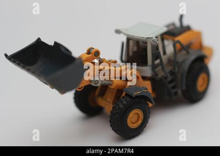 Nahaufnahme eines orangefarbenen Miniatur-Spielzeugs mit Radlader, isoliert auf weißem Hintergrund. Konzeptfoto eines schweren Miniaturspielzeugs. Stockfoto