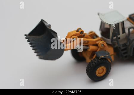 Nahaufnahme eines orangefarbenen Miniatur-Spielzeugs mit Radlader, isoliert auf weißem Hintergrund. Konzeptfoto eines schweren Miniaturspielzeugs. Stockfoto