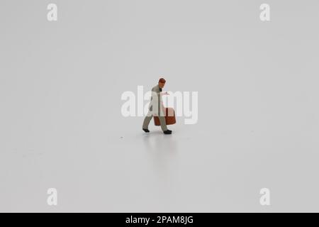 Nahaufnahme einer Miniaturfigur eines Büroangestellten, der einen Koffer auf weißem Hintergrund trägt. Miniaturfigur Fotokonzept. Stockfoto