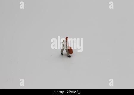 Nahaufnahme einer Miniaturfigur eines Büroangestellten, der einen Koffer auf weißem Hintergrund trägt. Miniaturfigur Fotokonzept. Stockfoto