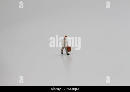 Nahaufnahme einer Miniaturfigur eines Büroangestellten, der einen Koffer auf weißem Hintergrund trägt. Miniaturfigur Fotokonzept. Stockfoto