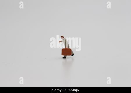 Nahaufnahme einer Miniaturfigur eines Büroangestellten, der einen Koffer auf weißem Hintergrund trägt. Miniaturfigur Fotokonzept. Stockfoto