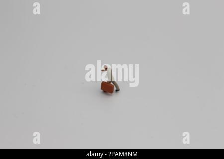 Nahaufnahme einer Miniaturfigur eines Büroangestellten, der einen Koffer auf weißem Hintergrund trägt. Miniaturfigur Fotokonzept. Stockfoto