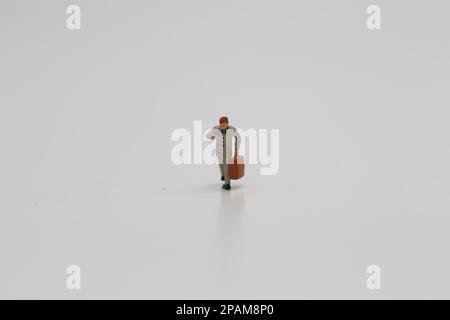 Nahaufnahme einer Miniaturfigur eines Büroangestellten, der einen Koffer auf weißem Hintergrund trägt. Miniaturfigur Fotokonzept. Stockfoto