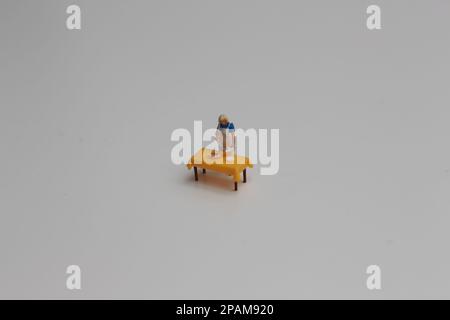 Nahaufnahme einer Miniaturfigur einer Frau, die Essen auf einem Tisch serviert, isoliert auf weißem Hintergrund. Miniaturfigur Fotokonzept. Stockfoto