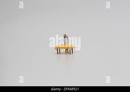 Nahaufnahme einer Miniaturfigur einer Frau, die Essen auf einem Tisch serviert, isoliert auf weißem Hintergrund. Miniaturfigur Fotokonzept. Stockfoto