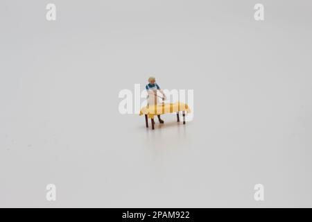 Nahaufnahme einer Miniaturfigur einer Frau, die Essen auf einem Tisch serviert, isoliert auf weißem Hintergrund. Miniaturfigur Fotokonzept. Stockfoto