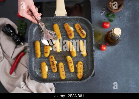 Mozzarella-Käsestifte werden in einer geölten Grillpfanne gebraten Stockfoto