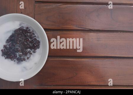 Nahaufnahme einer Schüssel mit schwarzem, klebrigem Reisbrei mit Kokosmilch zum Essen. Traditionelles indonesisches Speisenkonzept. Stockfoto