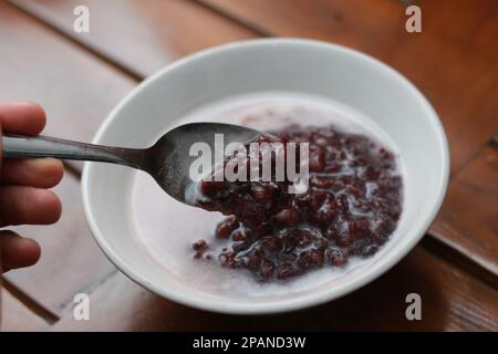 Nahaufnahme einer Schüssel mit schwarzem, klebrigem Reisbrei mit Kokosmilch zum Essen. Traditionelles indonesisches Speisenkonzept. Stockfoto