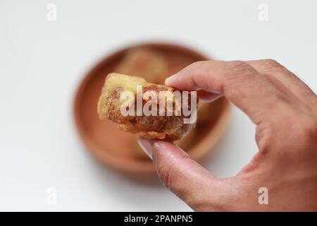 Nahaufnahme von gebratenem, gefülltem Tofu oder Gorengan Tahu ISI in der Hand isoliert auf weißem Hintergrund und Schüssel mit gefülltem, frittiertem Tofu verschwommen. Indonesisch f Stockfoto