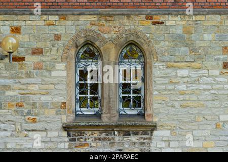 Steinwand eines alten Gebäudes mit zwei Bogenfenstern. Die Fenster sind mit dekorativem Metallgitter verschlossen. Laterne an der Wand. Stockfoto