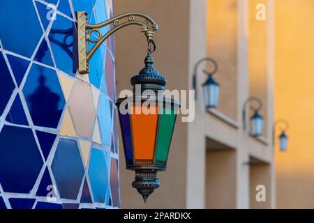 Mehrfarbige dekorative Straßenbeleuchtung im Freien, die an einer Mosaikwand befestigt ist. Schließen. Stockfoto