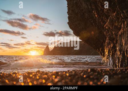 Meer Sonnenuntergang Wellen mit Schaum. Wellen fließen auf Kieseln und Felsen aus vulkanischem Basalt. Wasser zerfällt in Spritzer und weißen Schaum. Vor dem Hintergrund von Stockfoto