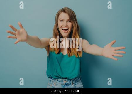 Eine freudige, aufgeregte Frau breitet ihre Arme aus, in der Hoffnung, jemanden zu umarmen, den man liebt und wichtig sieht, mit fröhlichstem Blick in die Kamera und breitem Zahnlächeln, ich Stockfoto