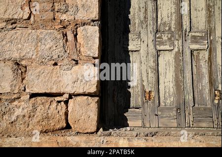 Antikes Fenster mit verwitterten Fensterläden aus Holz an einer handgefertigten Steinwand. Stockfoto