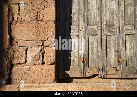 Antikes Fenster mit verwitterten Fensterläden aus Holz an einer handgefertigten Steinwand. Stockfoto