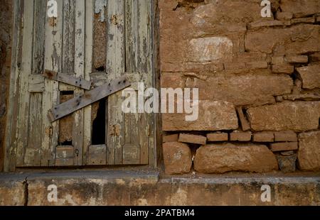 Antikes Fenster mit verwitterten Fensterläden aus Holz an einer handgefertigten Steinwand. Stockfoto