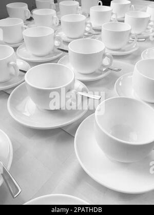 Viele Reihen weißer Keramikkaffee oder Teetassen. Schlangen an Kaffeetassen vor dem Konferenzraum. Weiße Keramikbecher und Untertassen auf einem Buffet Stockfoto