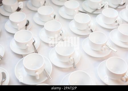 Viele Reihen weißer Keramikkaffee oder Teetassen. Schlangen an Kaffeetassen vor dem Konferenzraum. Weiße Keramikbecher und Untertassen auf einem Buffet Stockfoto