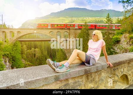 Frau auf der Solis-Viadukt-Brücke der Schweizer Eisenbahn in der Schweiz mit rotem Zug nach Pontresina. Schweizer Zug Bernina und Weltkulturerbe in Grisons. Albula Stockfoto