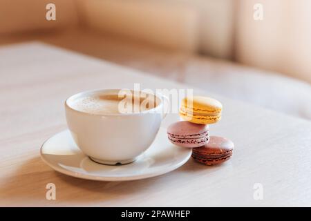 Eine Tasse Cappuccino-Kaffee, Makkaroni-Kuchen auf einem Tisch. Konzept von Frische und angenehmer Kühlung an einem heißen Tag. Karamellmakronen. Light flatley mit Stockfoto