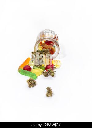 Verschiedene Gummis und getrocknete medizinische Marihuana-Knospen fielen aus dem geprägten Glasgefäß. Auf weißem Hintergrund. Viel Platz Stockfoto
