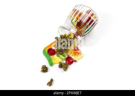 Verschiedene Gummis und getrocknete medizinische Marihuana-Knospen fielen aus dem geprägten Glasgefäß. Auf weißem Hintergrund. Viel Platz, Draufsicht Stockfoto