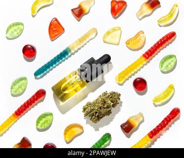 Unter kauender Marmelade verschiedener Formen, Geschmacksrichtungen und Farben liegen eine getrocknete Cannabisknospe und Flaschen Marihuanassamenöl in einem Muster auf einem weißen Backen Stockfoto