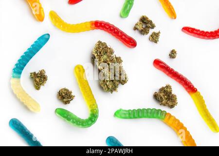 Getrocknete Marihuana-Knospen und Marmeladenwürmer verschiedener Farben liegen auf weißem Hintergrund. Blick von oben Stockfoto