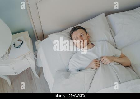 Blick von oben auf gestressten jungen weißen Mann, der mit offenen Augen im Bett lag und nicht schlafen konnte, der Mann sich unglücklich und müde von Schlaflosigkeit Stockfoto