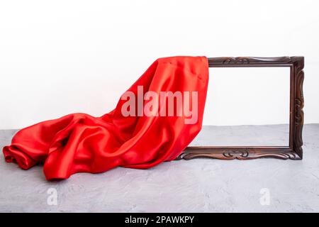 Rotes satiniertes Tuch mit braunem Holzrahmen auf Zementtisch und weißem Hintergrund, Modell zur Präsentation Stockfoto