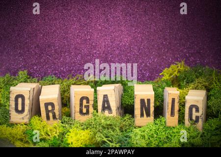 Organisches Wort auf Holzblöcken, mit Stempelschrift auf grüner Flechte mit lila satiniertem Hintergrund. Stockfoto