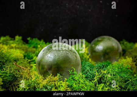 Zwei Glaskugeln auf grünem Flechten mit schwarzem Hintergrund, Nahaufnahme mit weichem Fokus Stockfoto