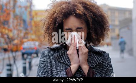 Kranke kranke afroamerikanische Frau mit lockigem Haar bläst laufende Nase in Papiertaschentücher draußen Kälteallergien Atemwegsvirus Mädchen leidet an Stockfoto