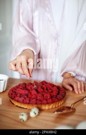 Nahaufnahme von Frauenhänden, die Himbeertorte dekorieren, köstlichen Kuchen mit frischen Beeren zubereiten Stockfoto