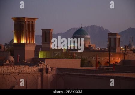 Beleuchtete Windtürme über den Dächern von Yazd, Iran, mit Bergen im Hintergrund Stockfoto